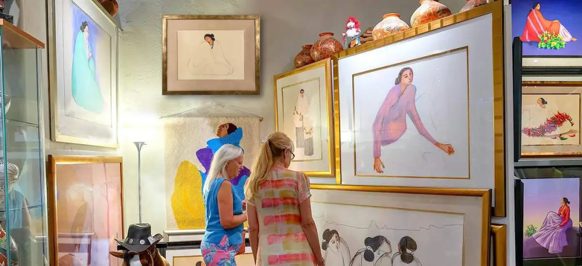 Two visitors view framed R.C. Gorman artwork and pottery in the gallery.